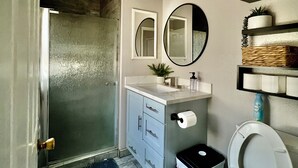 Un bagno con doccia, WC, lavabo con specchio e ripiano con articoli da toilette.
