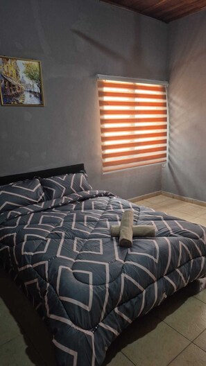 A bedroom with a bed, a window with blinds, a painting on the wall, and a wooden floor. - Luxury 3 bed house, closer to the beach and airport (Greater Accra Region)