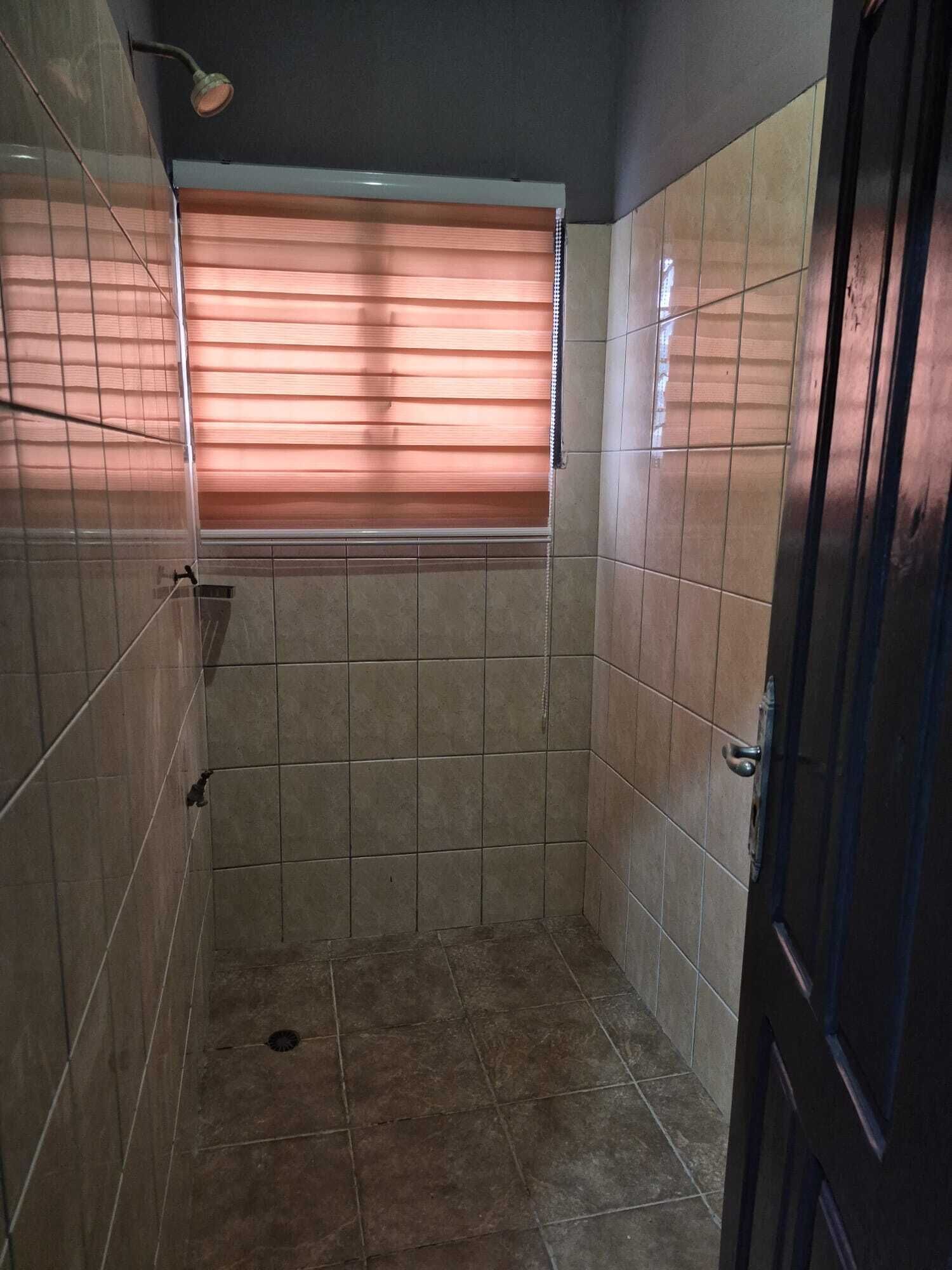 A small, tiled shower room with a window and a door.