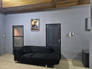 A room with a black sofa, a door, a framed picture, and a small cabinet. - Luxury 3 bed house, closer to the beach and airport (Greater Accra Region)