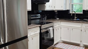 Una cocina moderna con armarios blancos, electrodomésticos de acero inoxidable, un horno negro y suelo de baldosas.