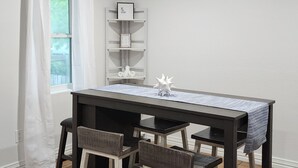 Un área de comedor con una mesa y sillas, una ventana con cortinas y una estantería decorada.