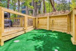 Ein Spielbereich aus Holz mit Kunstgrasanlage, einem Zaun und einer kleinen Gartenhütte.