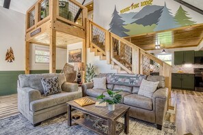 Ein Loft-Wohnbereich mit Treppe, zwei Sofas, einem Couchtisch und einem Wandbild, das einen Wald zeigt.