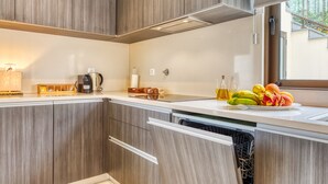 Eine moderne Küche mit Holzschränken, einem integrierten Geschirrspüler, einer Kaffeemaschine und einer Obstschale auf der Arbeitsplatte.