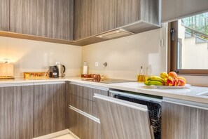 Eine moderne Küche mit Holzschränken, einem integrierten Geschirrspüler, einer Kaffeemaschine und einer Obstschale auf der Arbeitsplatte.