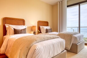 Ein Hotelzimmer mit zwei Betten, einem großen Fenster mit Blick und einem Nachttisch mit Lampe.
