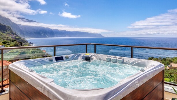 Ein Whirlpool mit weitem Meerblick, einer Holzterrasse und wolkenlosem Himmel.