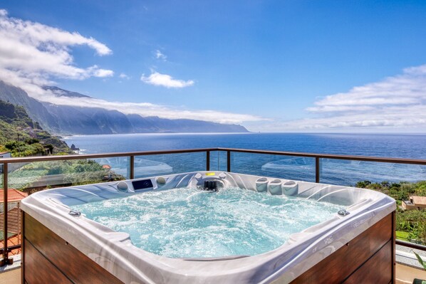 Ein Whirlpool mit weitem Meerblick, einer Holzterrasse und wolkenlosem Himmel.