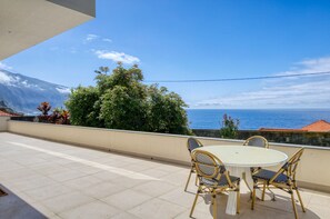 Ein Balkon mit rundem Tisch und Stühlen, Blick auf das Meer und ein Berg im Hintergrund.