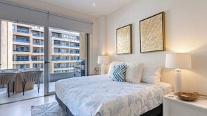 Ein Schlafzimmer mit einem Bett, zwei Nachttischlampen, einem Nachttisch, einem großen Fenster und Blick auf ein Gebäude.