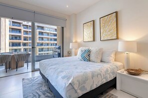 Ein Schlafzimmer mit einem Bett, zwei Nachttischlampen, einem Nachttisch, einem großen Fenster und Blick auf ein Gebäude.