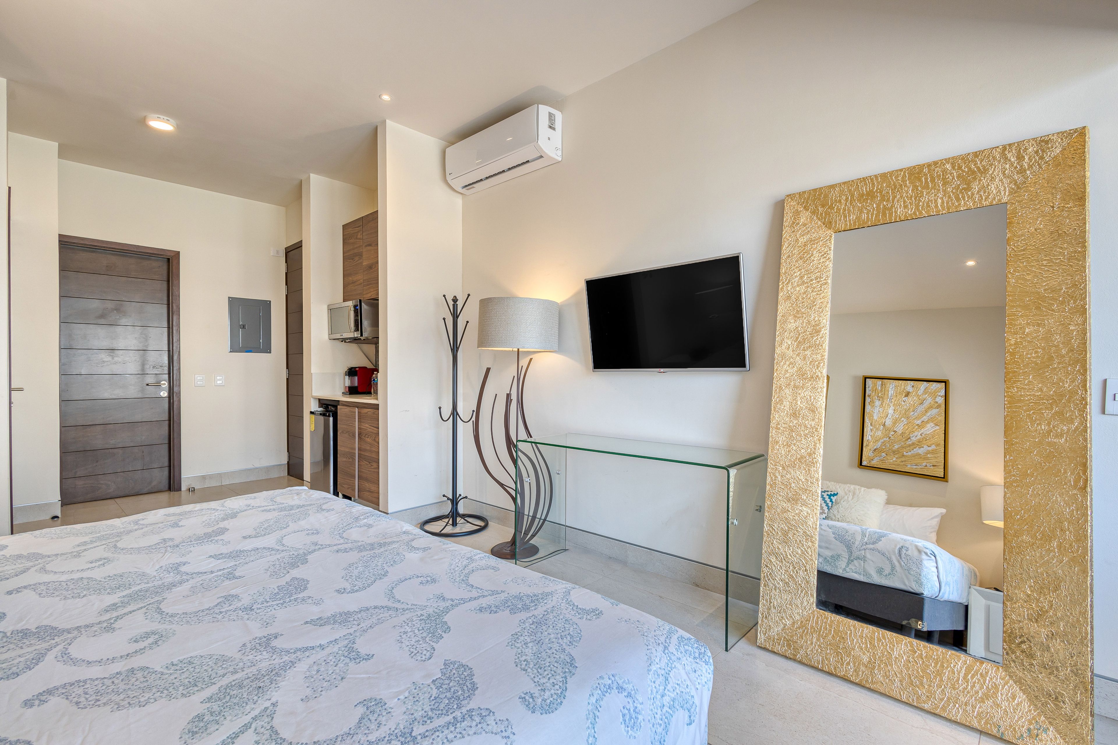 Une chambre d’hôtel moderne dotée d’un grand lit, d’un téléviseur fixé au mur, d’un grand miroir avec un cadre doré et d’un téléviseur à écran plat.