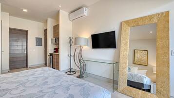 Une chambre d’hôtel moderne dotée d’un grand lit, d’un téléviseur fixé au mur, d’un grand miroir avec un cadre doré et d’un téléviseur à écran plat.
