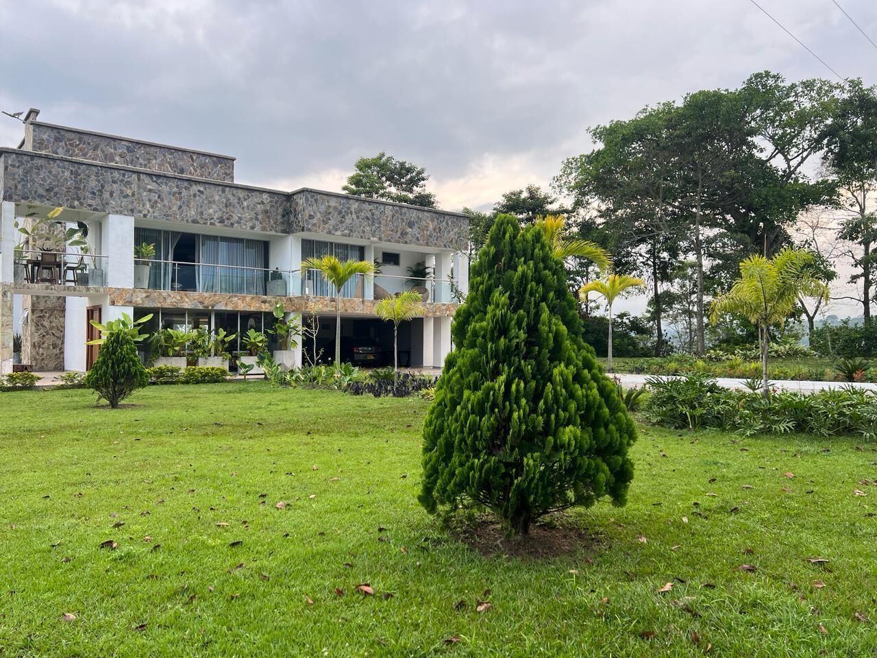 A modern building with a stone facade, a covered outdoor seating area, and a well-maintained lawn with a conical tree.