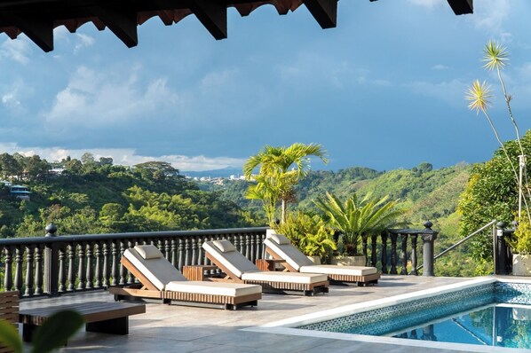 A rooftop pool area with lounge chairs and a view of a lush landscape.