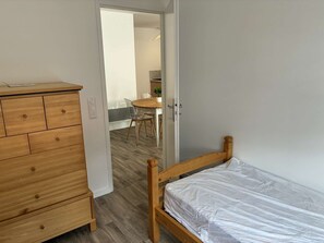 Una camera da letto con un letto e una cassettiera in legno, e un'area pranzo visibile attraverso una porta aperta.