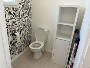 Un bagno con il water, un rotolo di carta igienica, un mobiletto contenitore e una parete decorata.