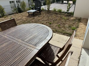 Un tavolo rotondo in legno con sedie, un giardino erboso, una recinzione e un edificio sullo sfondo.
