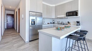 A modern kitchen with a stainless steel refrigerator, a microwave, and a large island with bar stools. - Stunning Oceanfront Luxury Apartment With Spacious Balcony Perfect for Families (Cabo San Lucas)