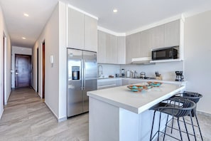 Eine moderne Küche mit einem Edelstahlkühlschrank, einer Mikrowelle und einer großen Kochinsel mit Barhocker.