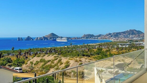 A balcony with a clear view of the ocean, palm trees, and distant mountains. - Stunning Oceanfront Luxury Apartment With Spacious Balcony Perfect for Families (Cabo San Lucas)