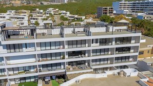 A multi-story hotel with balconies, a rooftop pool, and a green lawn area. - Stunning Oceanfront Luxury Apartment With Spacious Balcony Perfect for Families (Cabo San Lucas)