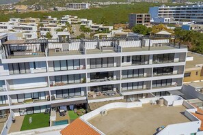 Ein mehrstöckiges Hotel mit Balkonen, einem Pool auf dem Dach und einer Grünfläche.