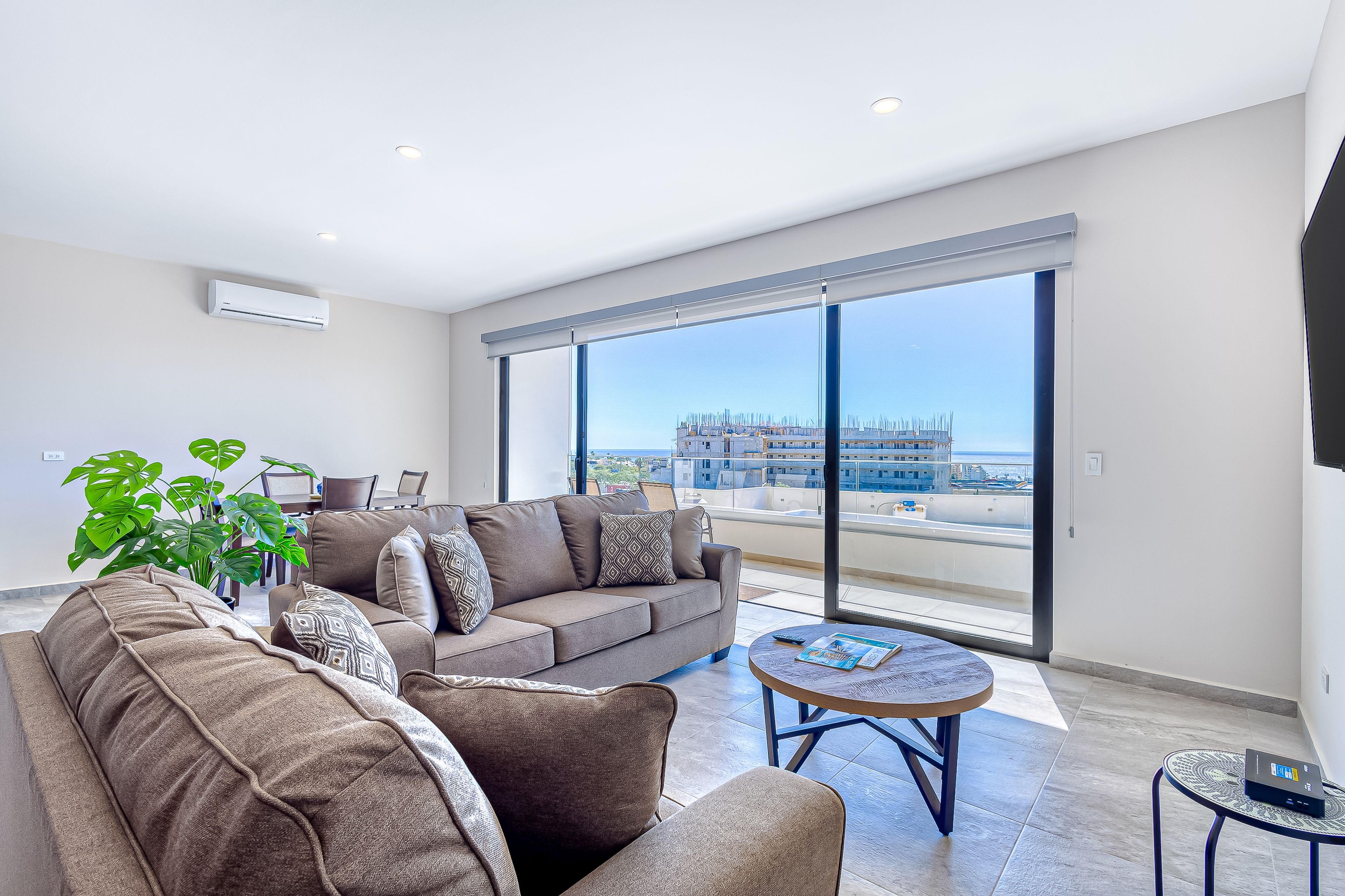 Una sala de estar moderna con un sofá, una mesa de centro y un ventanal que ofrece vistas a una obra en construcción.