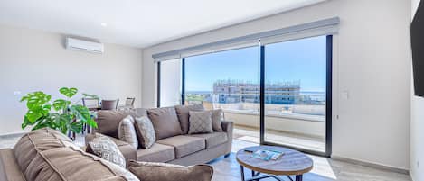 A modern living room with a sofa, coffee table, and a large window offering a view of a construction site.