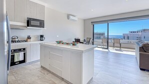 A modern kitchen with a central island, a dining area with a view, and a living space with a sofa and chairs. - Stunning Oceanfront Luxury Apartment With Spacious Balcony Perfect for Families (Cabo San Lucas)