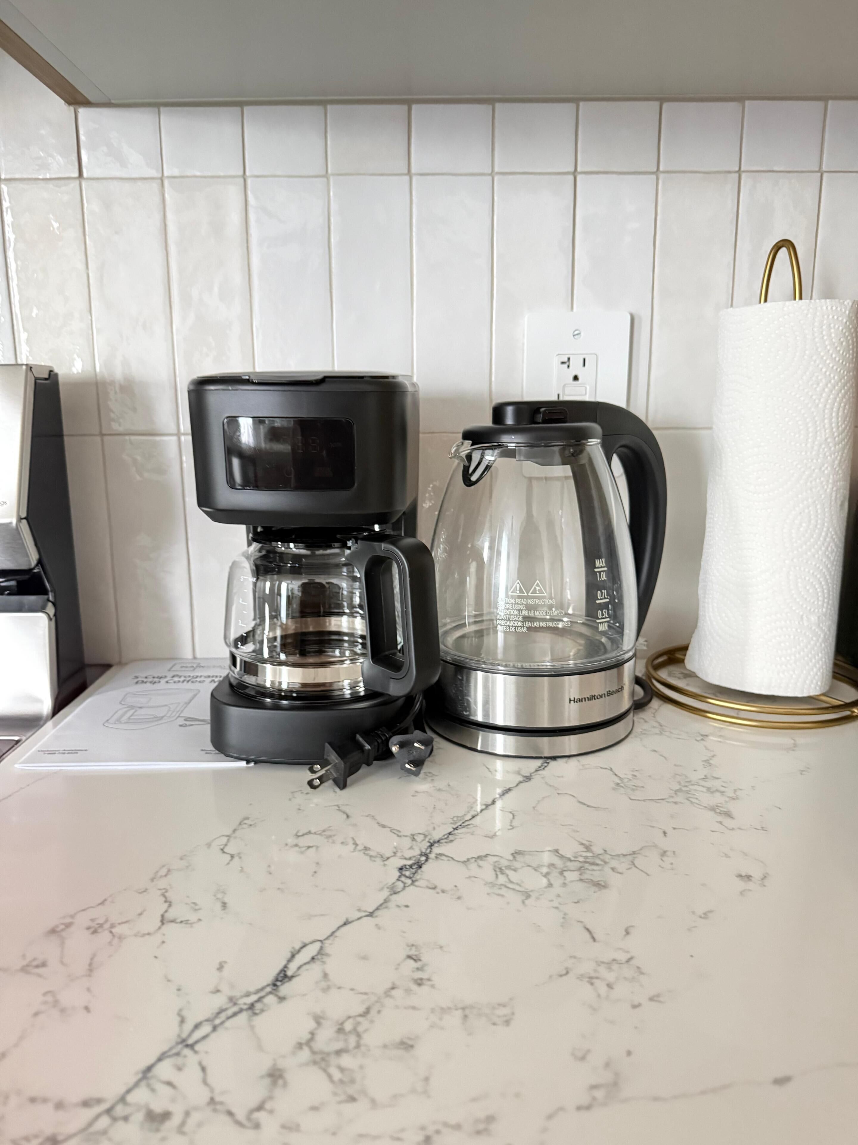 Eine Kaffeemaschine, eine Glaskaraffe und ein Papiertuchspender auf einer Marmorarbeitsplatte.