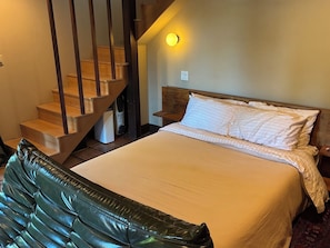 A bedroom with a bed, a wooden staircase, a nightstand, and a wall-mounted light.