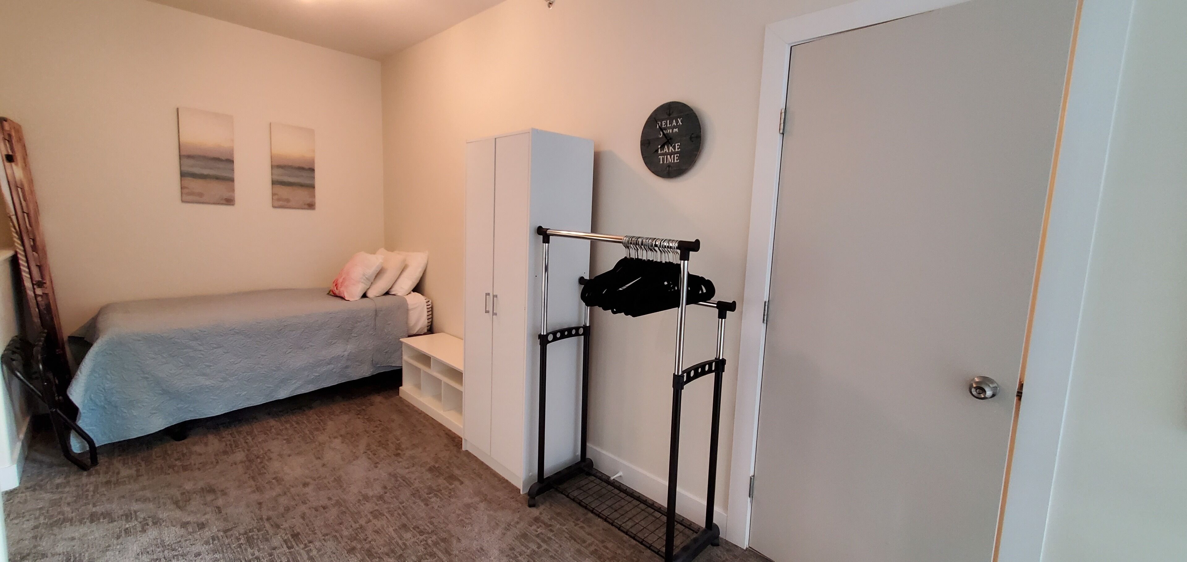 A bedroom with a bed, a wardrobe, a coat rack, and a wall clock.