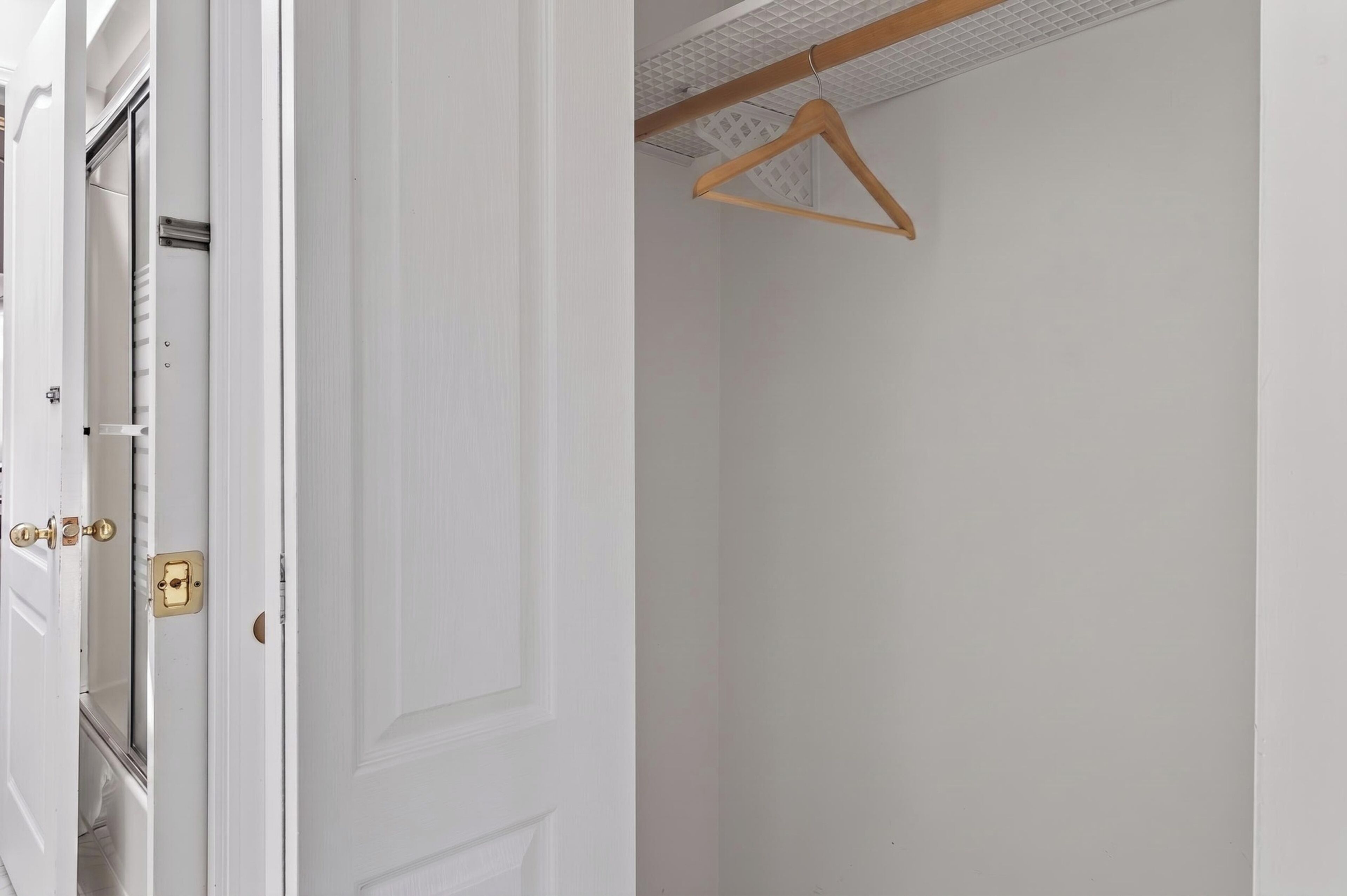 Uma porta branca com fechadura de latão e um cabide de madeira na parede.