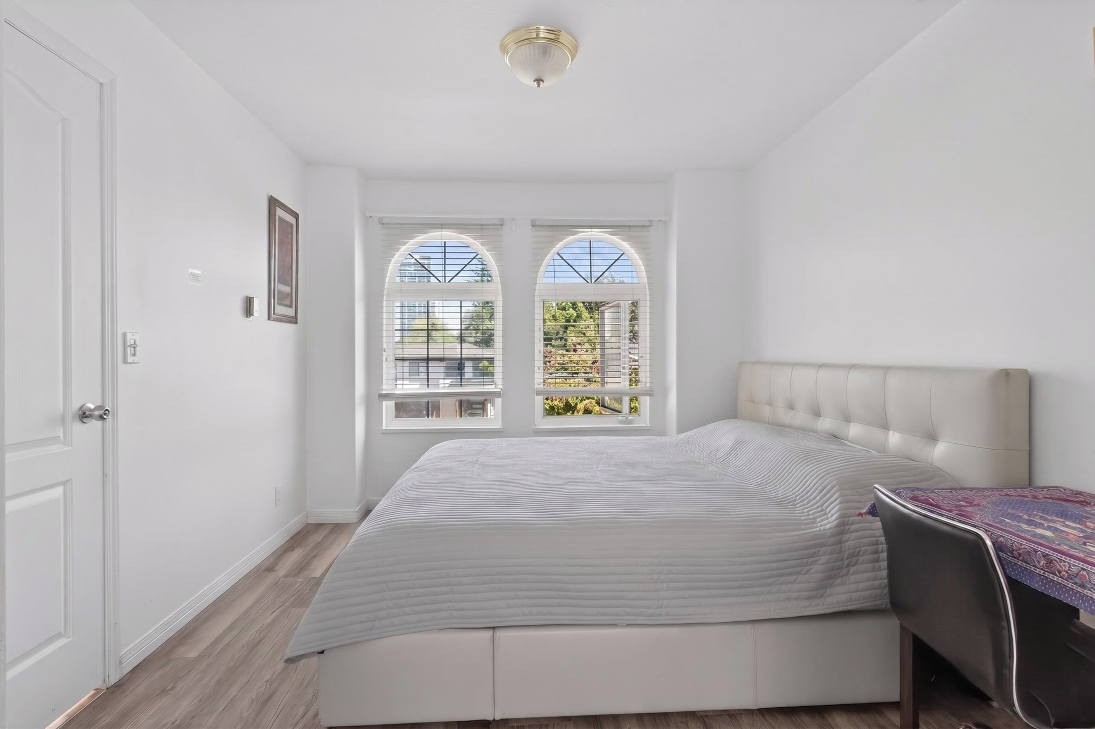 Un dormitorio con cama, una silla, una puerta y dos ventanas con vistas.