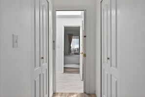 A hallway with white doors leading to a bedroom with a bed and a window. - Deer Lake Suite Rooms 201 + 203 in Burnaby Metrotown area near Skytrain and shop (Burnaby)