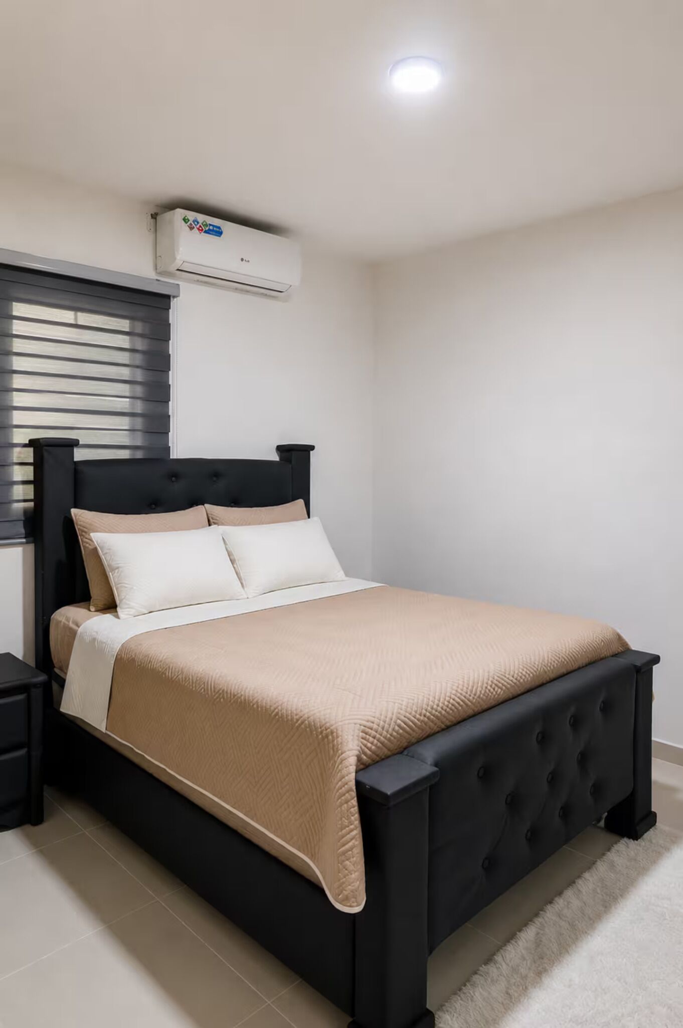 A bed with a black headboard, beige bedding, and an air conditioning unit on the wall.