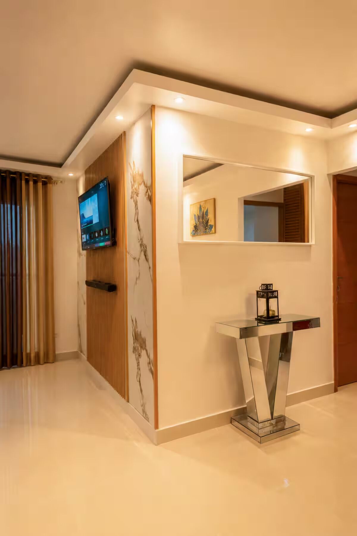 Una moderna hall d'albergo con una TV a schermo piatto, uno specchio decorativo e un tavolino con piano in vetro.