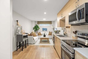 A modern kitchen with a microwave, oven, and sink. There is a dining area with a table and chairs. - The Royal Bay Stay,  by Victoria Prime! (Victoria)