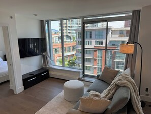 Ein modernes Schlafzimmer mit großem Fenster, Flachbildfernseher, Sofa und Nachttisch.