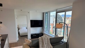 Una camera d'albergo moderna con un letto grande, un divano, una televisione e vista sulla città.