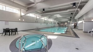 Un'ampia piscina coperta con corsie ben delimitate, una zona relax con tavoli e sedie, e un cartello con le regole della spa affisso al muro.