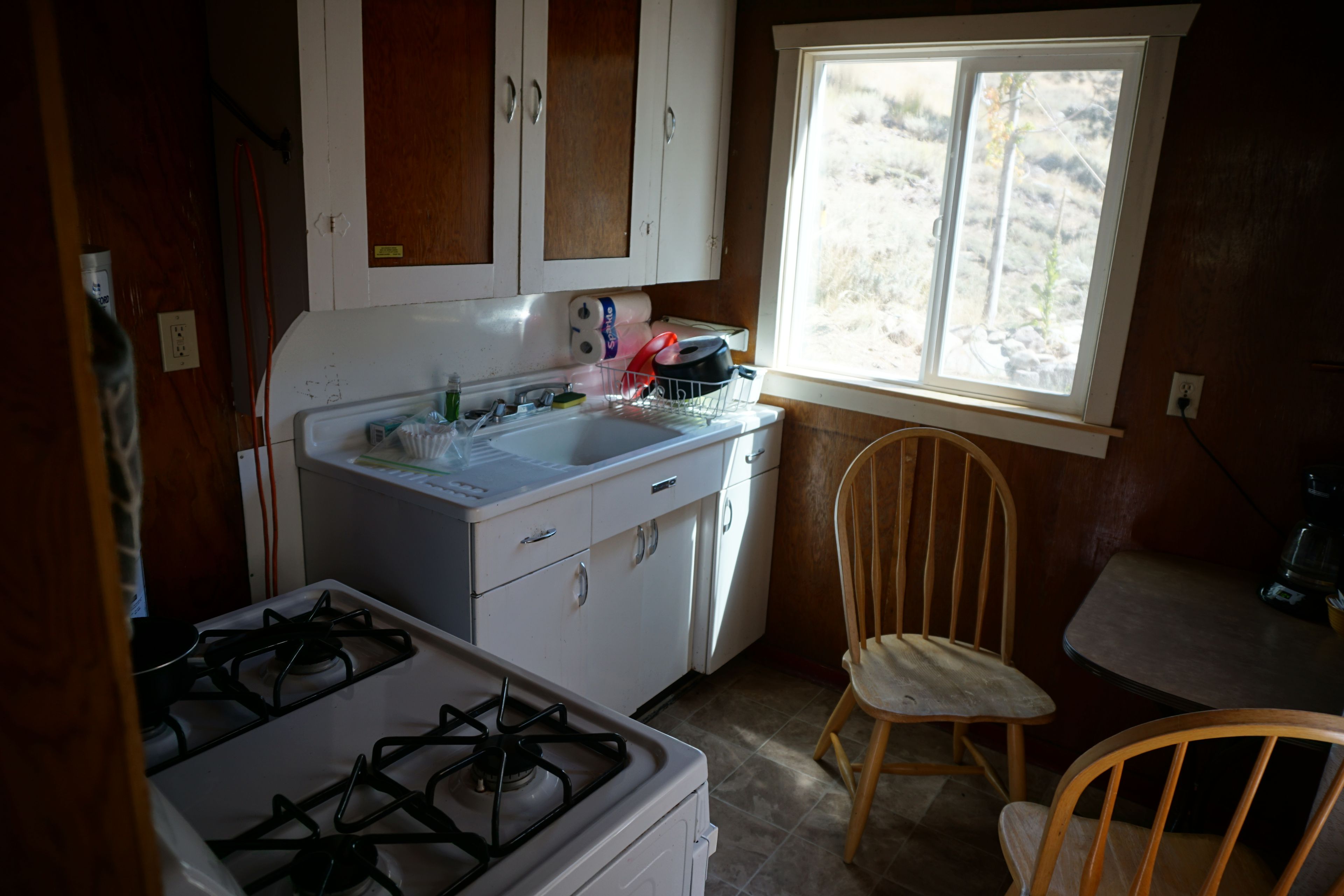 Une cuisine compacte équipée d’une cuisinière à gaz, d’un évier et d’une fenêtre donnant sur un paysage naturel.