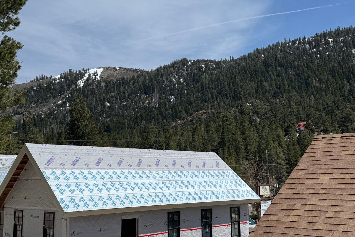 A building with a white exterior and a patterned roof, surrounded by a forested mountain backdrop.
