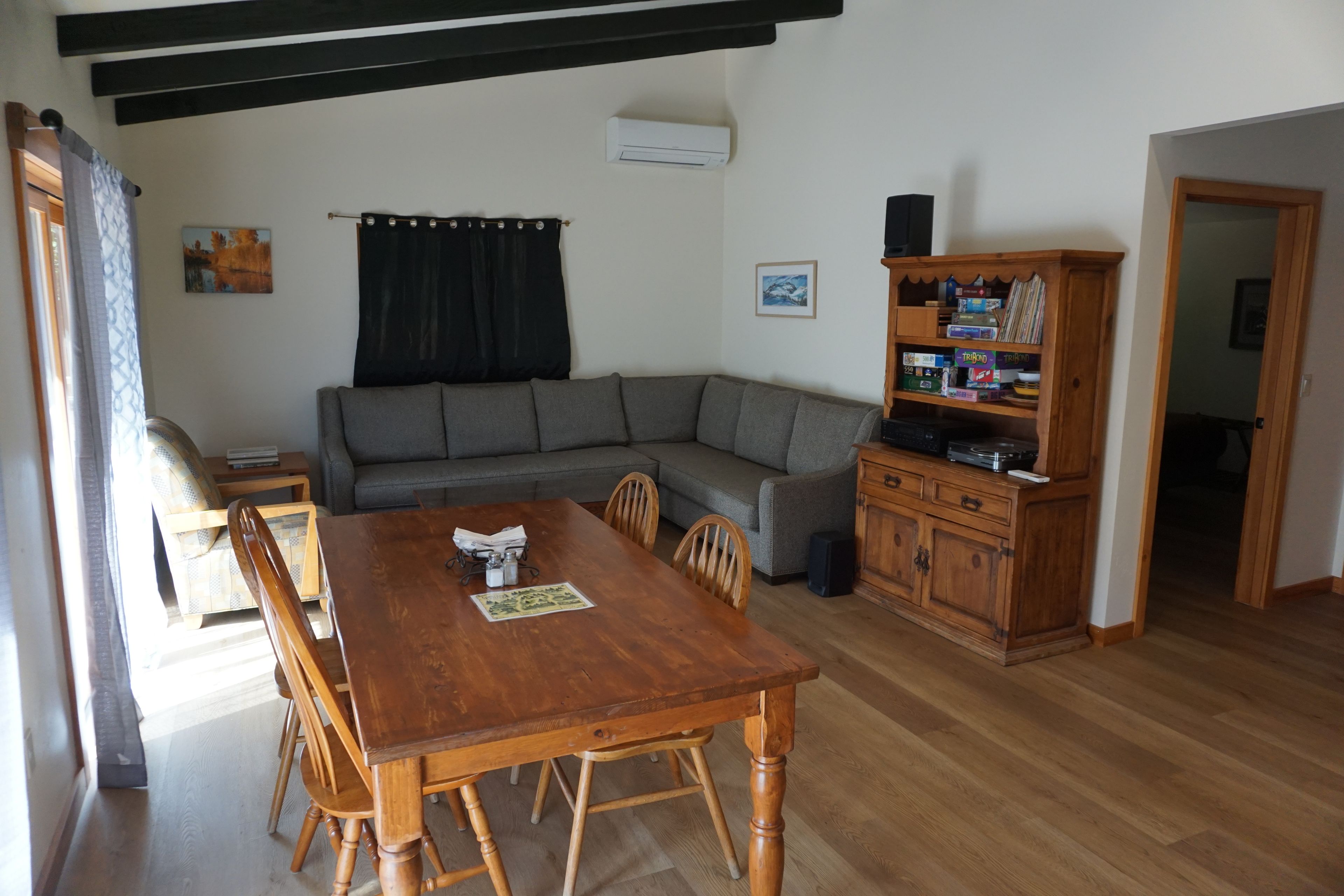 A living room with a wooden dining table, grey sofa, and a wooden cabinet with board games.