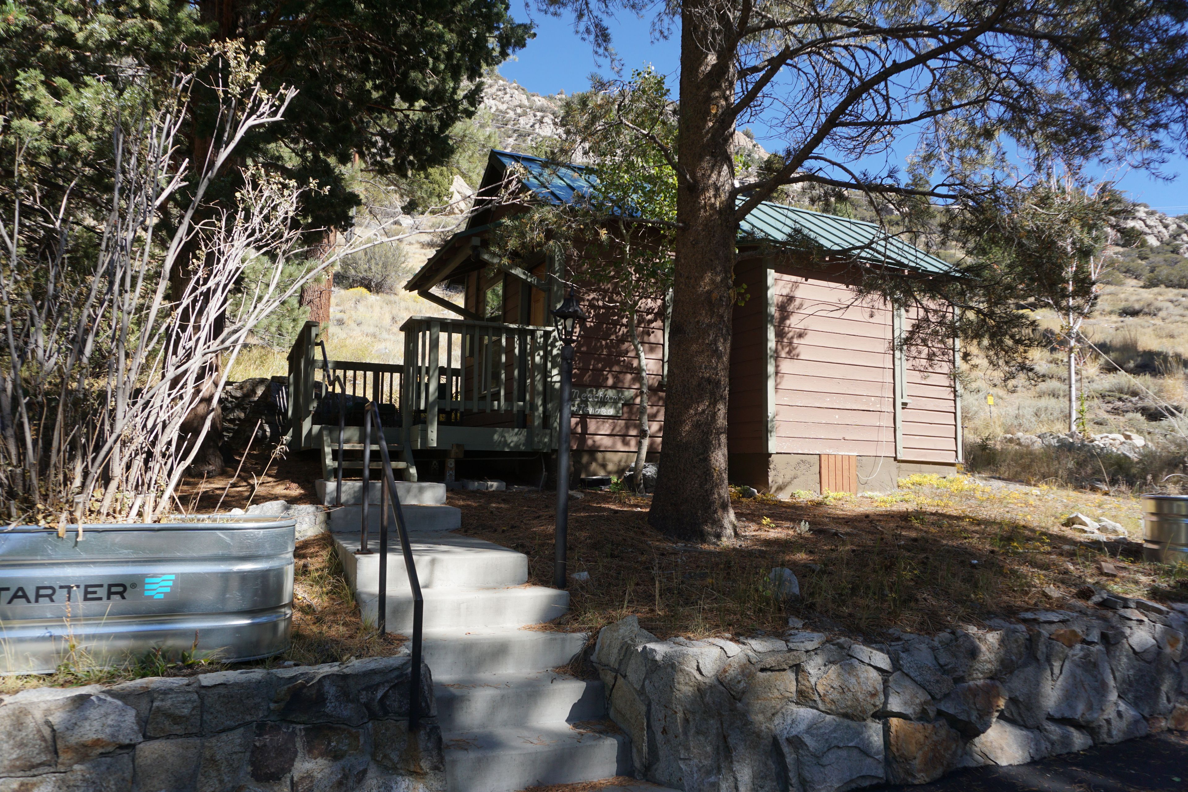 A cabin with a wooden deck, stone steps, and a metal barrel labeled 'TARTER'.