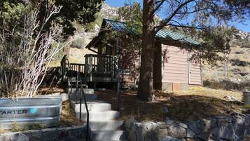 A cabin with a wooden deck, stone steps, and a metal barrel labeled 'TARTER'.
