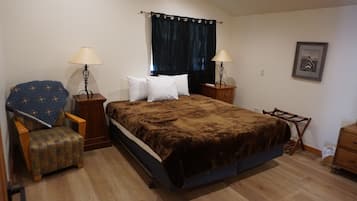 Un dormitorio con una cama grande, dos mesitas de noche, una silla, un pequeño mueble y una lámpara, además de un cuadro en la pared.