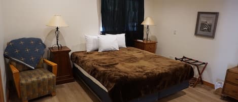 A bedroom with a large bed, two bedside tables, a chair, a nightstand, a lamp, and a framed picture on the wall.